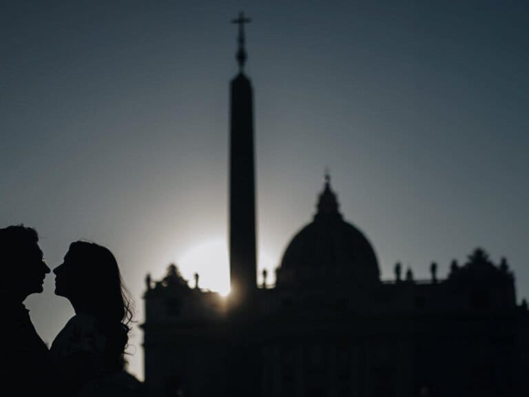 Silhouettes of a couple facing each other during their Rome Pre Wedding photoshoot, with the sun setting behind them and the outline of St. Peter’s Basilica and an obelisk in the background.