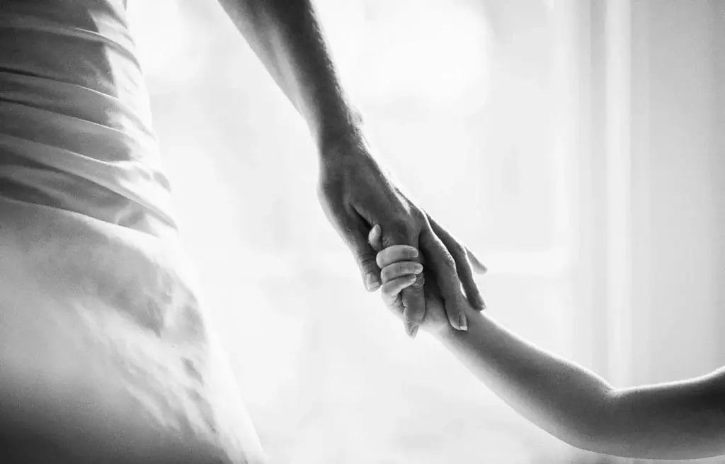 A black and white photo captures the essence of Yorkshire wedding photography, as an adult gently clasps a childs hand. Both are reaching out, bathed in soft lighting that creates a warm and tender atmosphere.