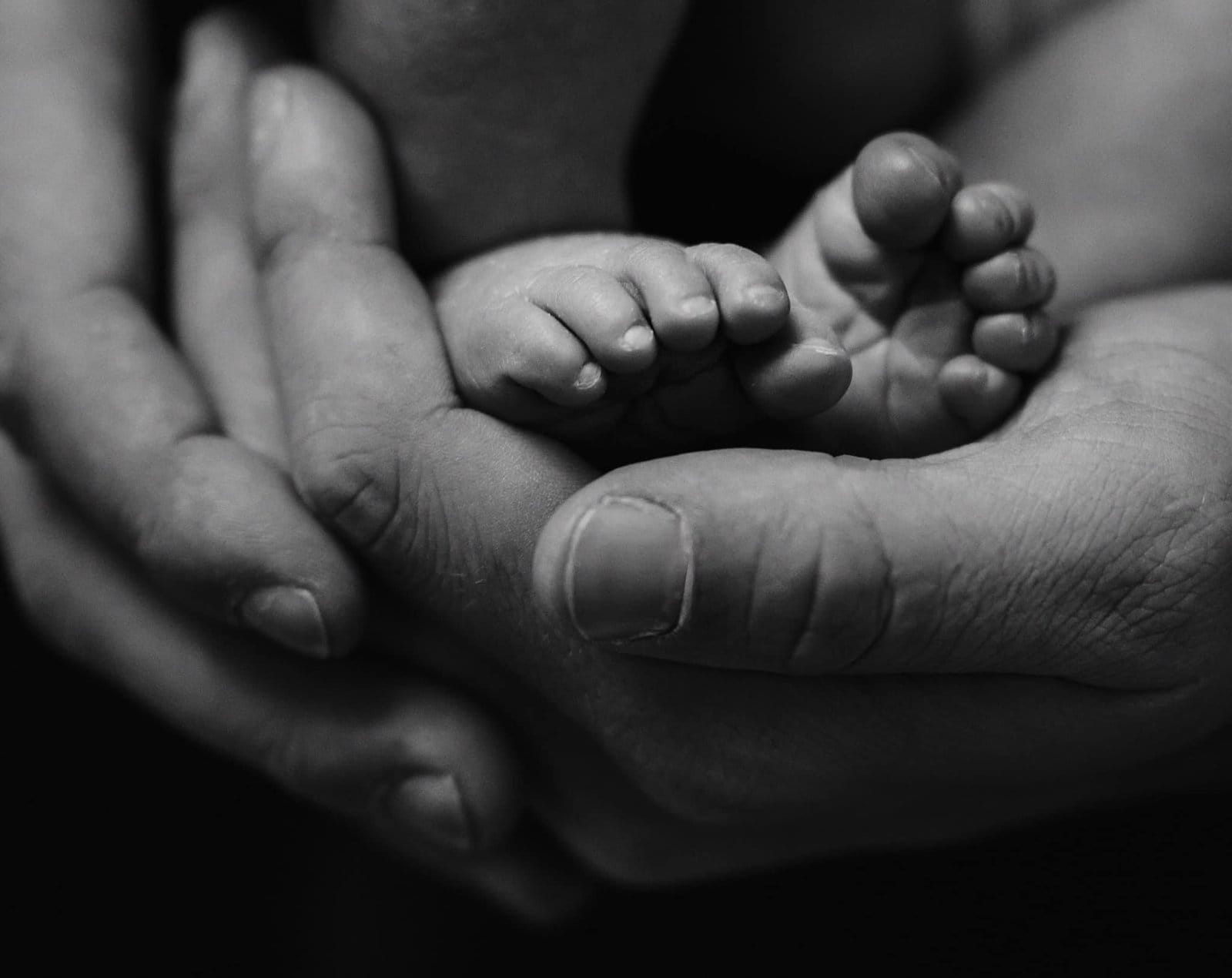 Close-up black and white image by a Yorkshire newborn baby photographer captures adult hands gently cradling a newborns tiny feet, creating a serene and tender scene.