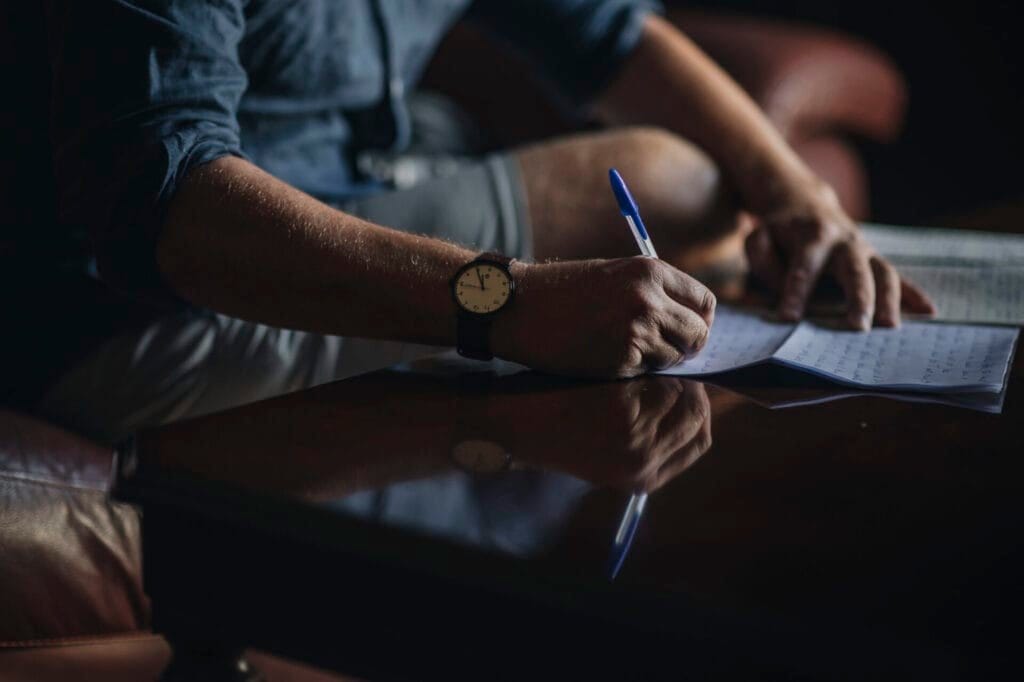 In the dimly lit ambiance of a dark wooden table, a person adorned with a watch writes with a pen on paper, capturing thoughts as delicately as a wedding photographer in Italy. The scene evokes the charm of Villa Palazzola, hidden in the romance that Rome always promises.
.