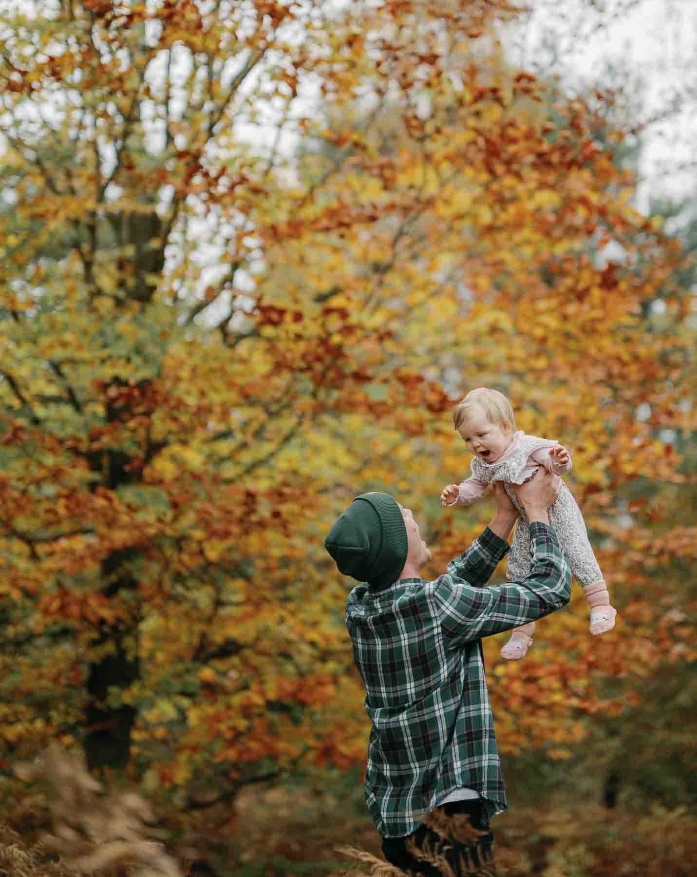 father and young daughter playing infront of autumn trees