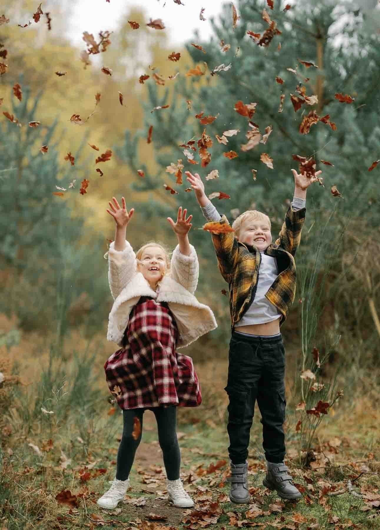 2 young children laughng and throwing autumn leaves