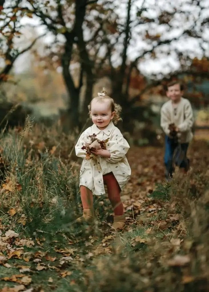 little girl playing with autumn leaves with her brotehr behind. yorkshire family photoshoot in clumber park at autumn
