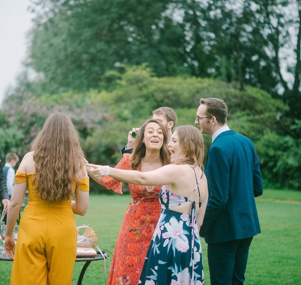 A group of people gather outdoors on a lush green lawn. They are dressed in vibrant, formal attire, suggesting a festive event. With trees and bushes as a backdrop, Hornington Manor wedding photographer captures the lively and joyful atmosphere perfectly.